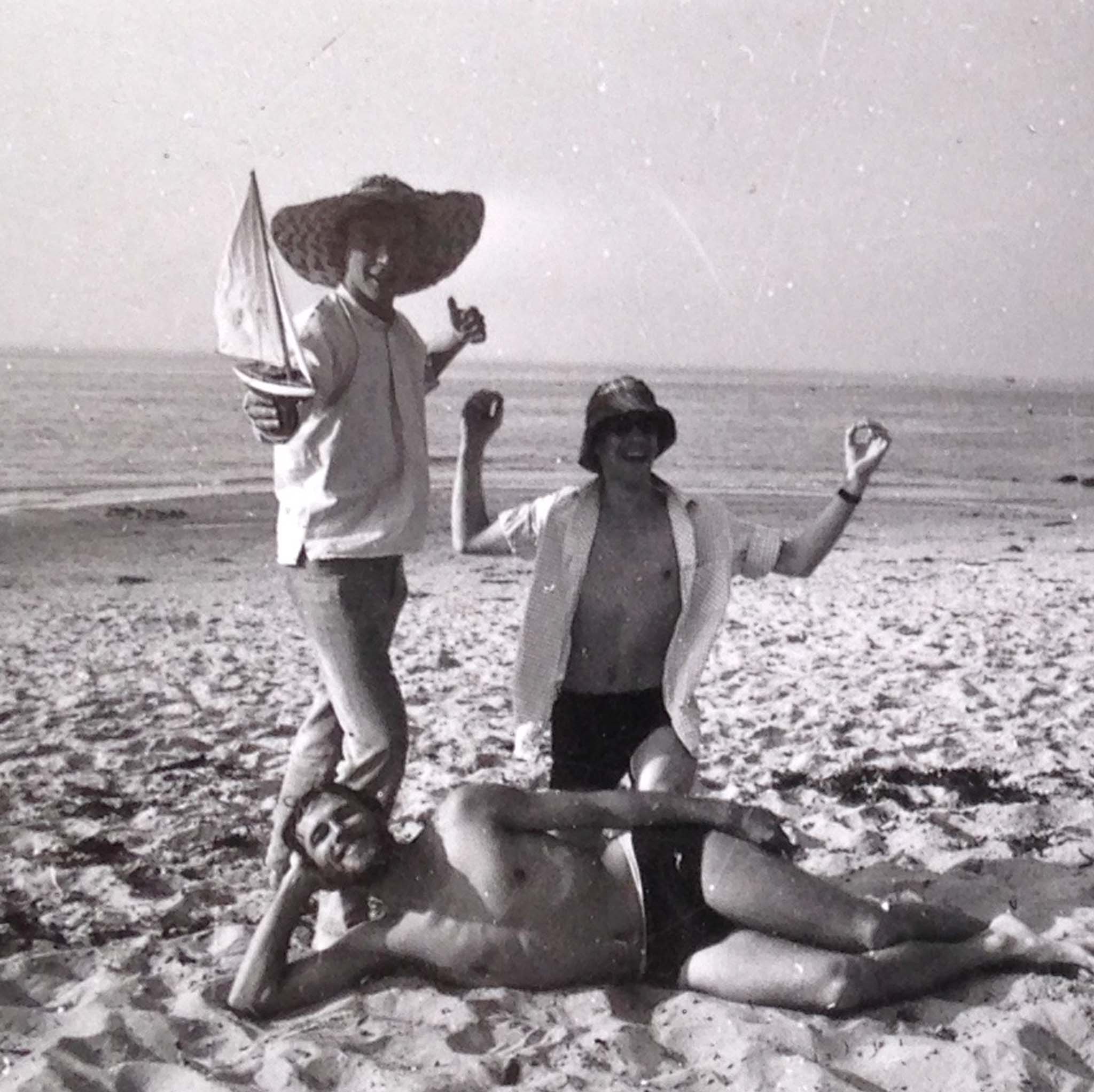 Sommerbillede i sort-hvid af Thomas Winding og venner ved havet med båd og hatte.
