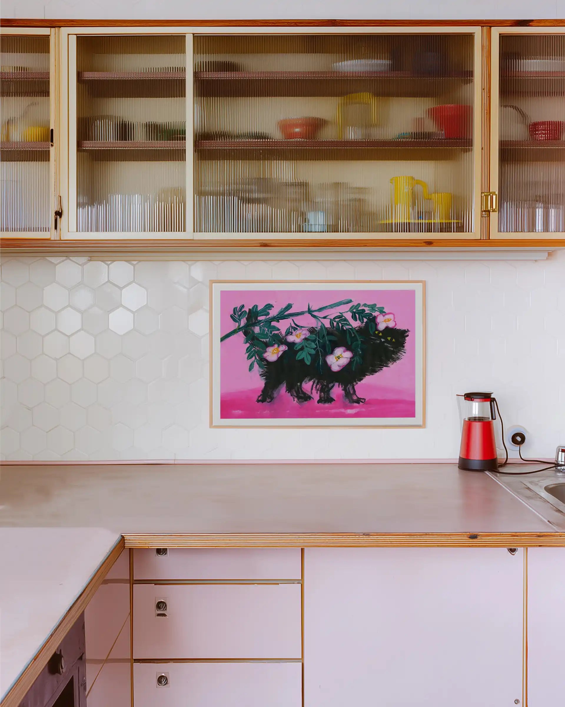 Plakat “Pimme under roserne” af Thomas Winding ophængt i køkken med lyse fliser, træskabe og rolig indretning.