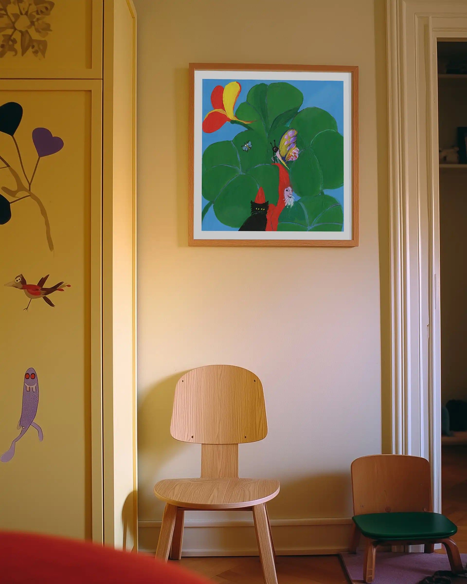 Plakat “Den hemmelige have” af Thomas Winding ophængt i hyggeligt børneværelse med stole, garderobe og varme farver.