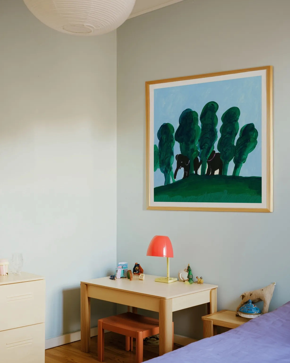 Børneværelse med rolig indretning og farverig kunstplakat med elefanter og grønne træer, hængende over et lille skrivebord.