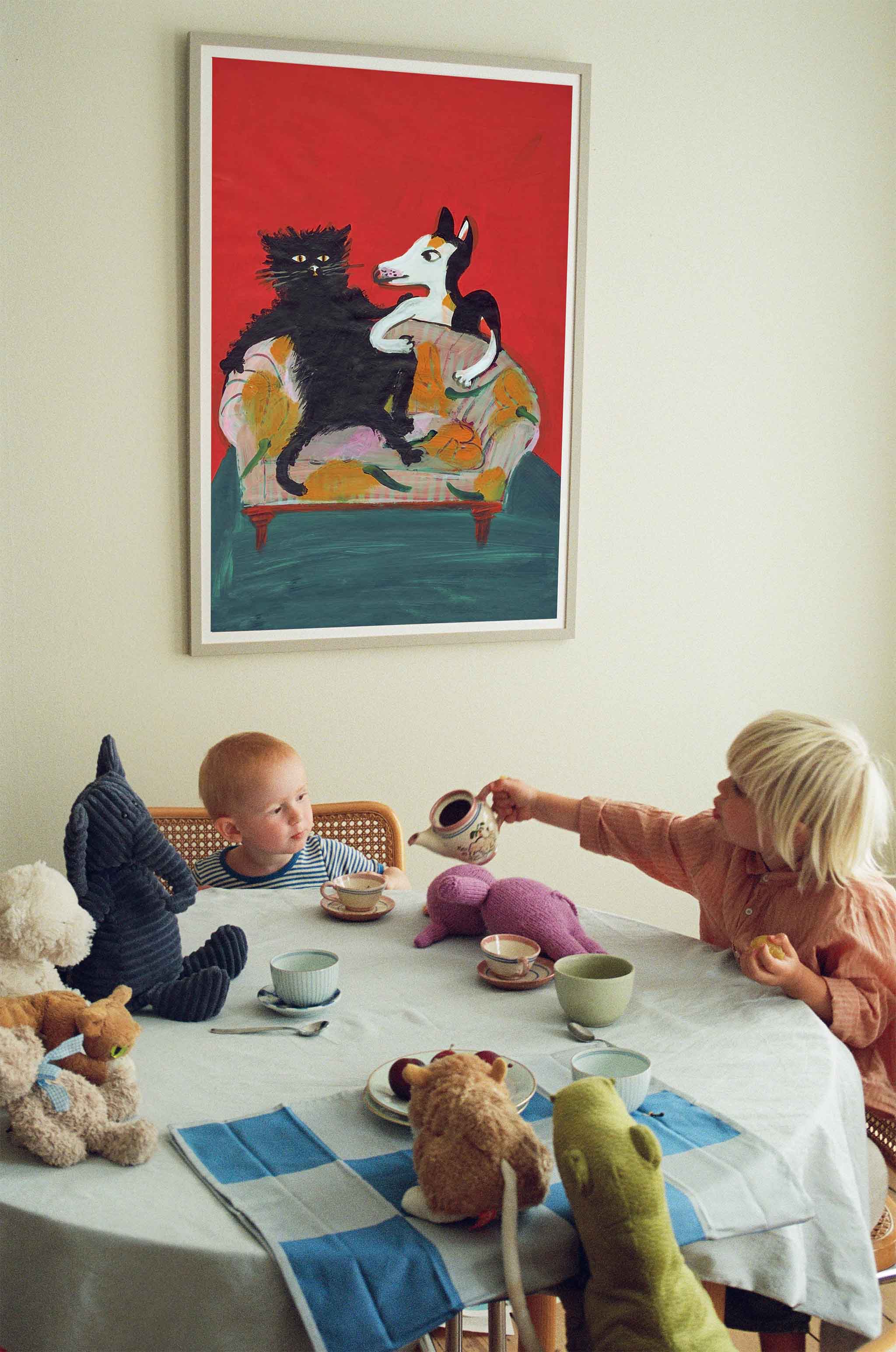 Plakat af Thomas Winding med farverig illustration af kat og hund i sofa – kunst til børneværelse og stue. På billedet leger børn teselskab med tøjdyr under plakaten