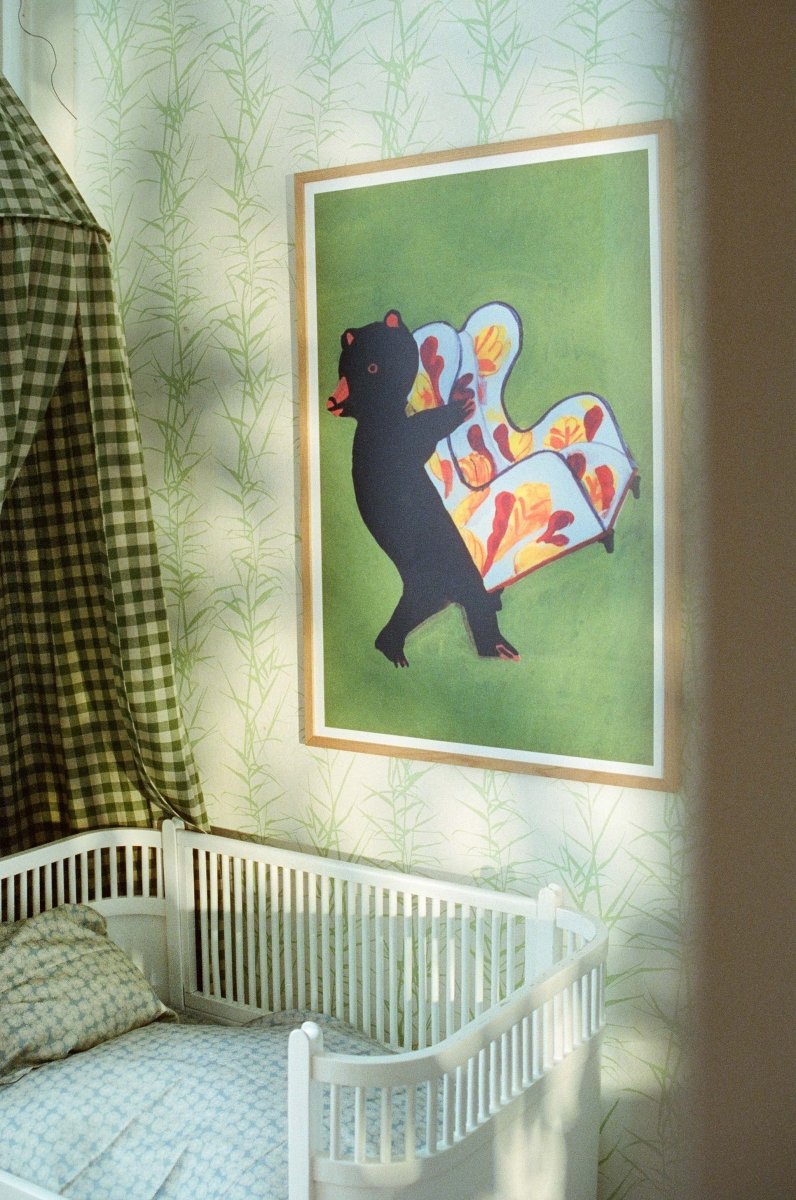 Plakat “Lænestolens lange rejse” af Thomas Winding ophængt i børneværelse med tremmeseng, bløde tekstiler og rolig stemning.